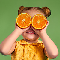 Young girl holding orange slices over her eyes